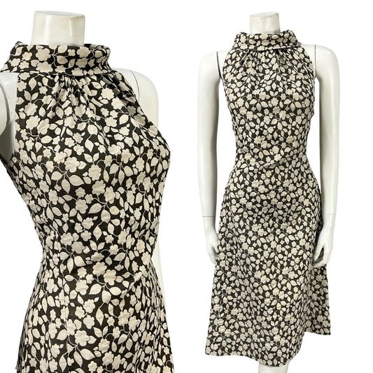 Mannequin wears a cream and black floral print halter funnel neck mini dress. 
